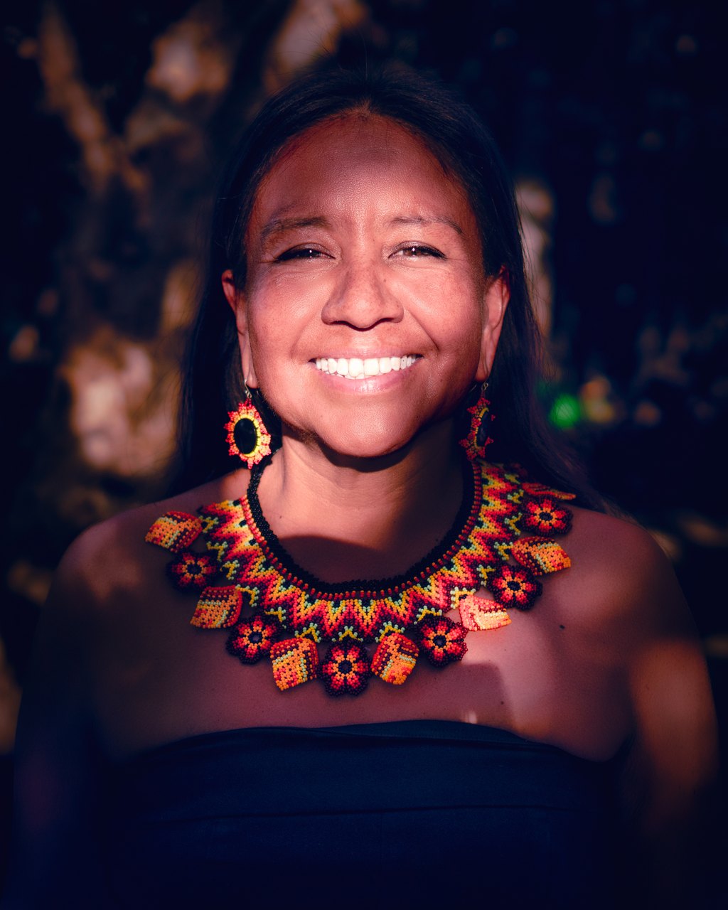 Portrait of a smiling woman wearing a colorful beaded necklace.