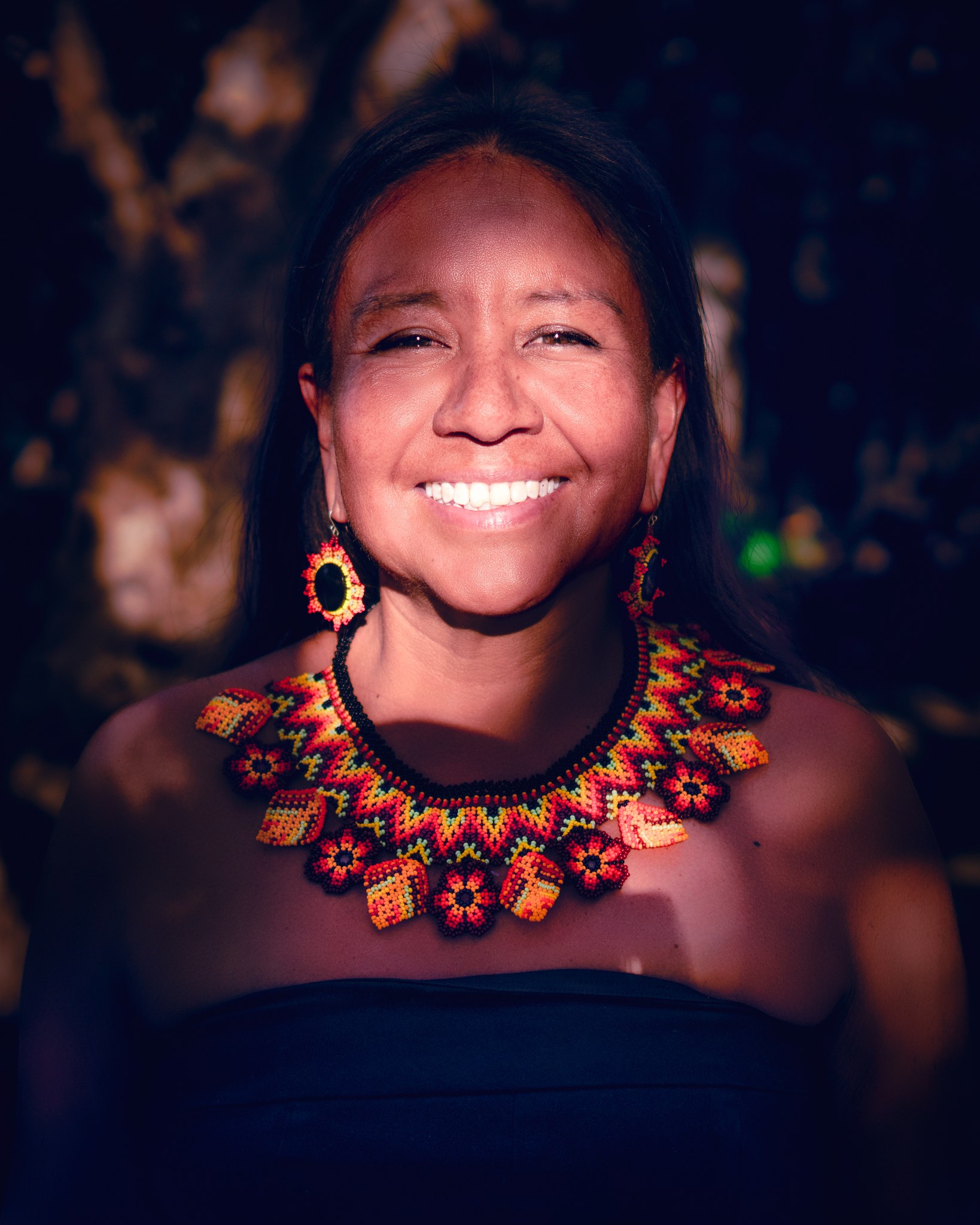 Portrait of a smiling woman wearing a colorful beaded necklace.